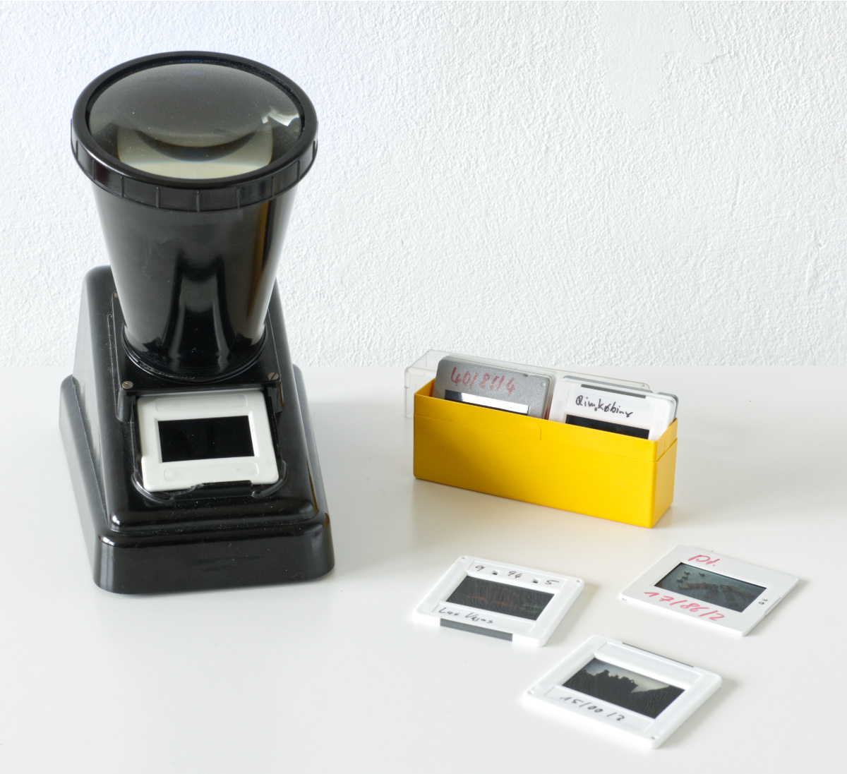 Fast quadratisches Farbfoto, das einen alten, schwarzen Diabetrachter und ein gelbes Kästchen mit einigen Dias zeigt.