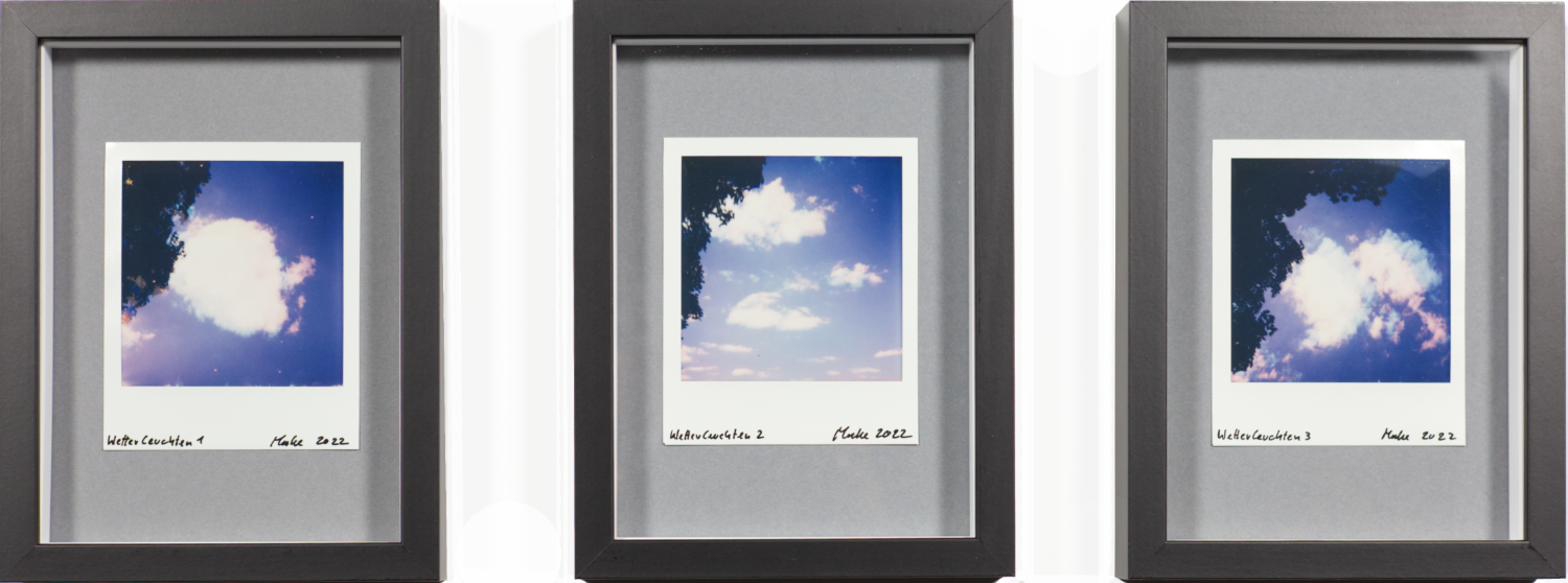Drei einzeln stehende Bilder von in schwarzen Objektrahmen auf grauem Karton montierten Polaroidbildern. Die Bilder zeigen jeweils Wolken vor einem blauen Himmel und changieren an den Rändern farblich zwischen blau und rot.